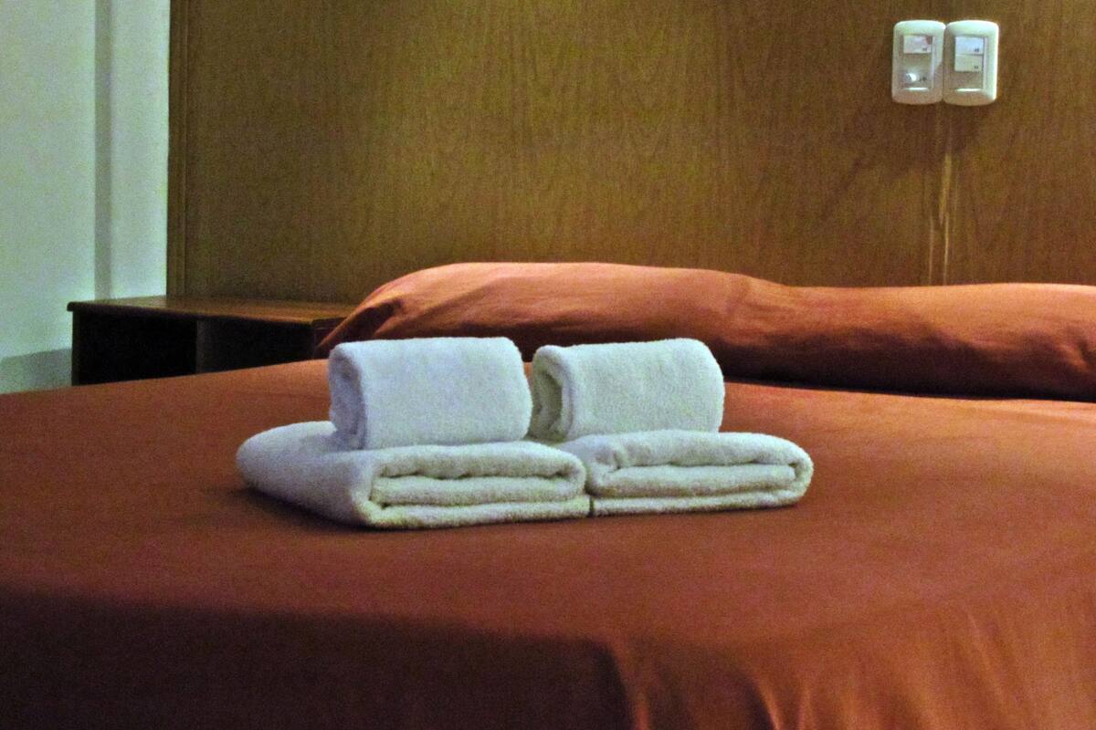 A neatly made bed with two folded towels and a wooden headboard.