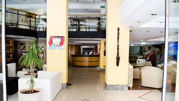 A hotel lobby with a reception desk, seating area, and a staircase to an upper level.
