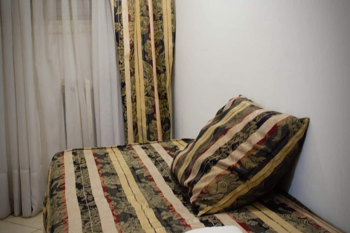 A bed with a striped bedspread and a pillow, a white towel on the bed, and a window with curtains.