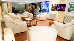 A spacious lobby with multiple seating areas, a reception desk, and a television screen.