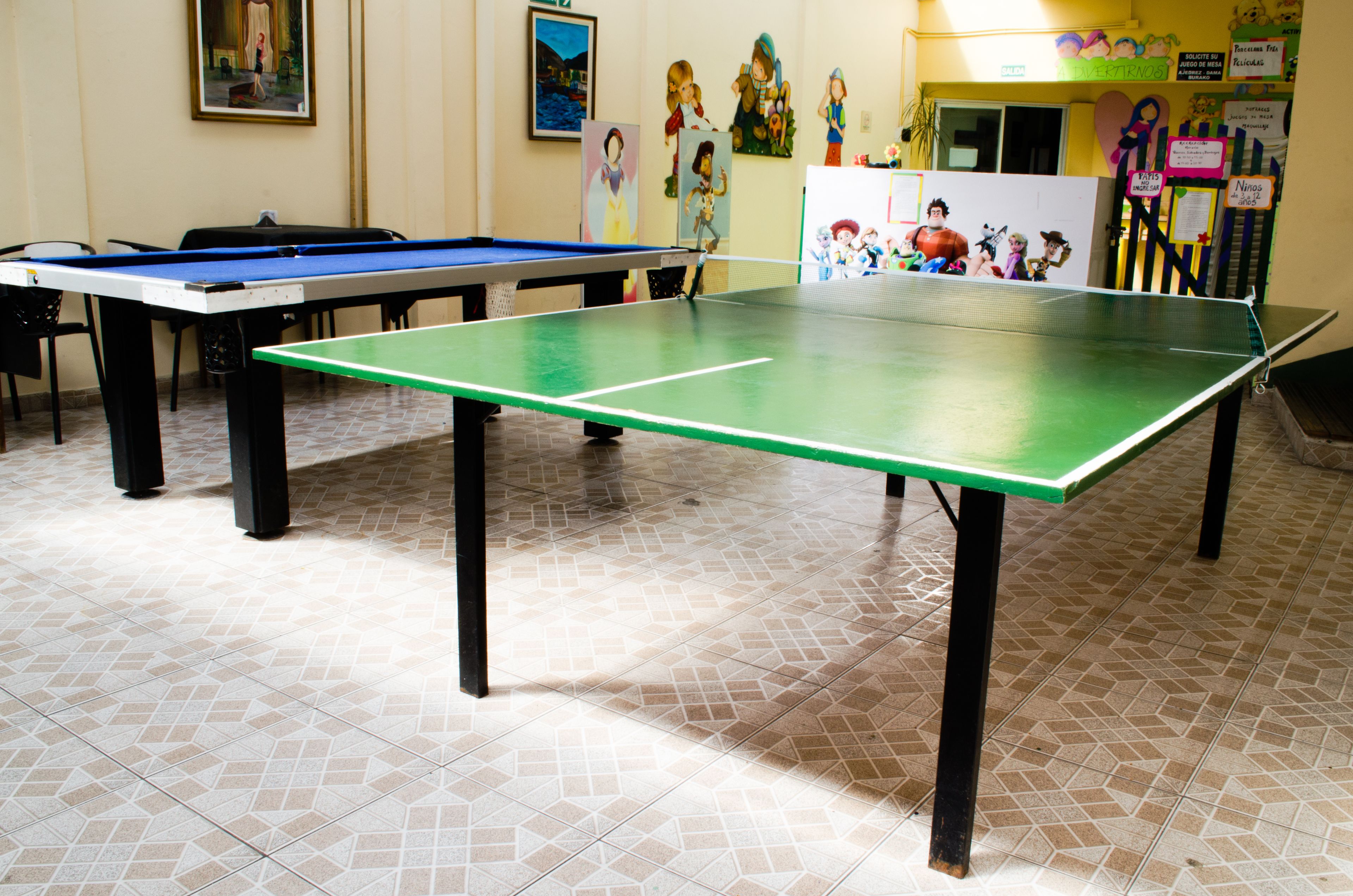 A billiards table with a green playing surface and black legs, surrounded by a tiled floor.