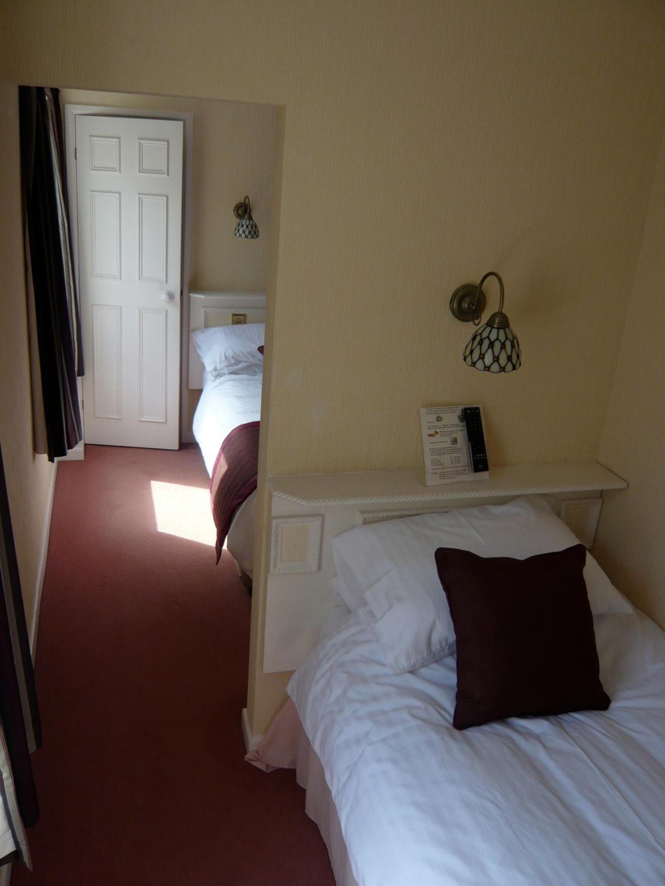 A hotel room with a bed, a nightstand, a lamp, and a door leading to another room.