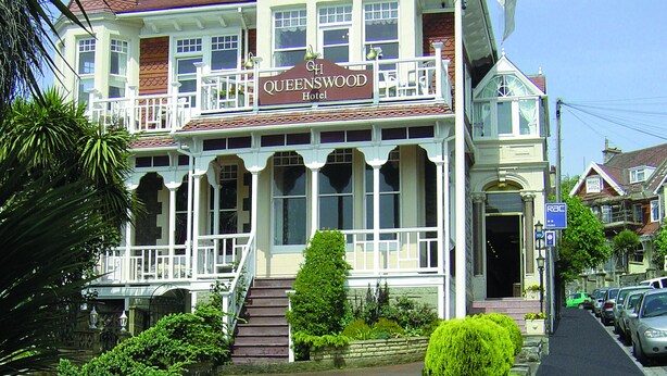 A historic hotel with a prominent balcony, a well-maintained garden, and a clear blue sky. - Queenswood Hotel (Weston-super-Mare)