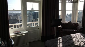 A bedroom with a bed, a chair, a radiator, and a window with curtains. - Queenswood Hotel (Weston-super-Mare)