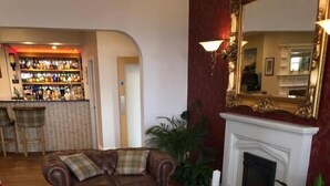 A living room with a fireplace, a bar area, and a seating arrangement including a brown leather sofa and armchairs. - Queenswood Hotel (Weston-super-Mare)