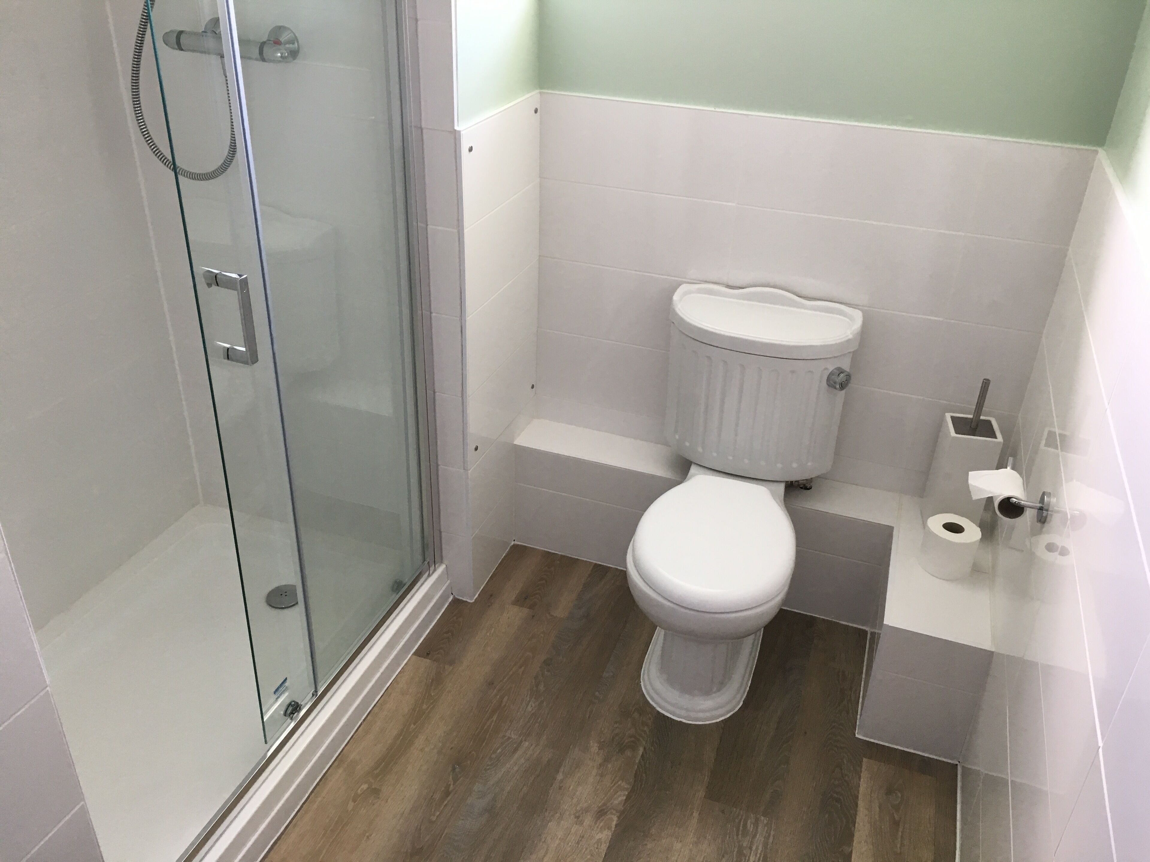 A bathroom with a glass shower enclosure, a toilet, and a small sink area.