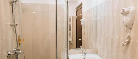 Casa de banho com cabine de duche em vidro, lavatório e secador de cabelo fixado na parede.