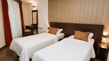 Una habitación de hotel con dos camas individuales, un escritorio con silla, un espejo y una mesita de noche con lámpara.