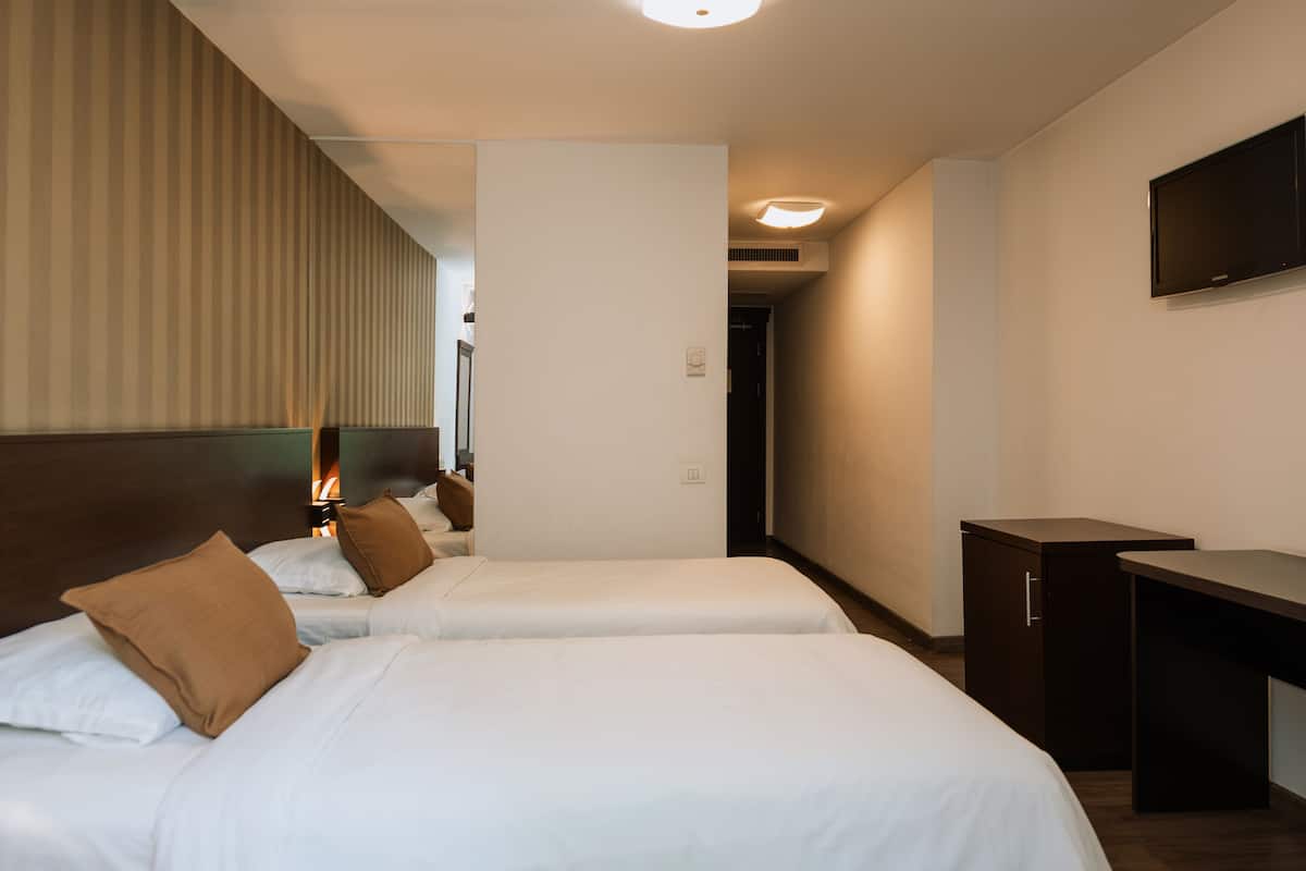 A hotel room with two beds, a desk, a television, and a door leading to another room.