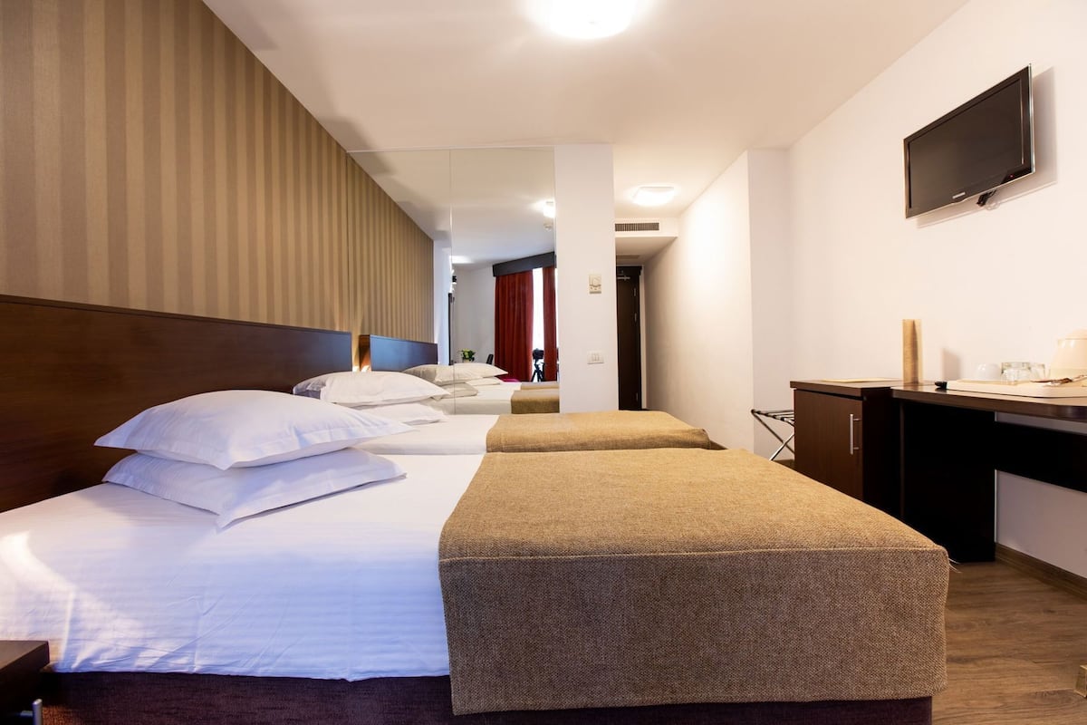 A hotel room with two beds, a desk, a flat-screen TV, and a kitchenette.