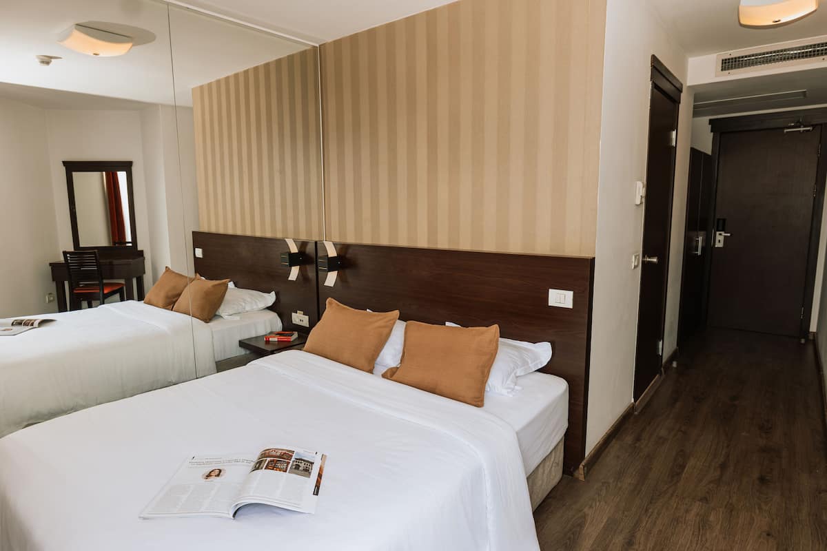 A hotel room with two beds, a nightstand, a mirror, and a wooden headboard.