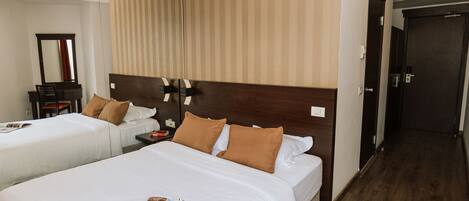 Une chambre d’hôtel avec deux lits, une table de chevet, un miroir et une tête de lit en bois.