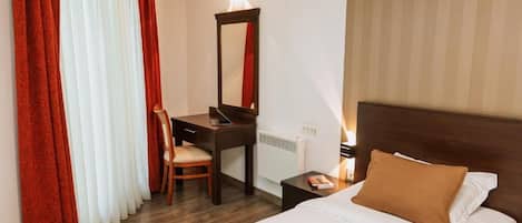 A hotel room with a bed, a desk, a chair, a nightstand, and a mirror.