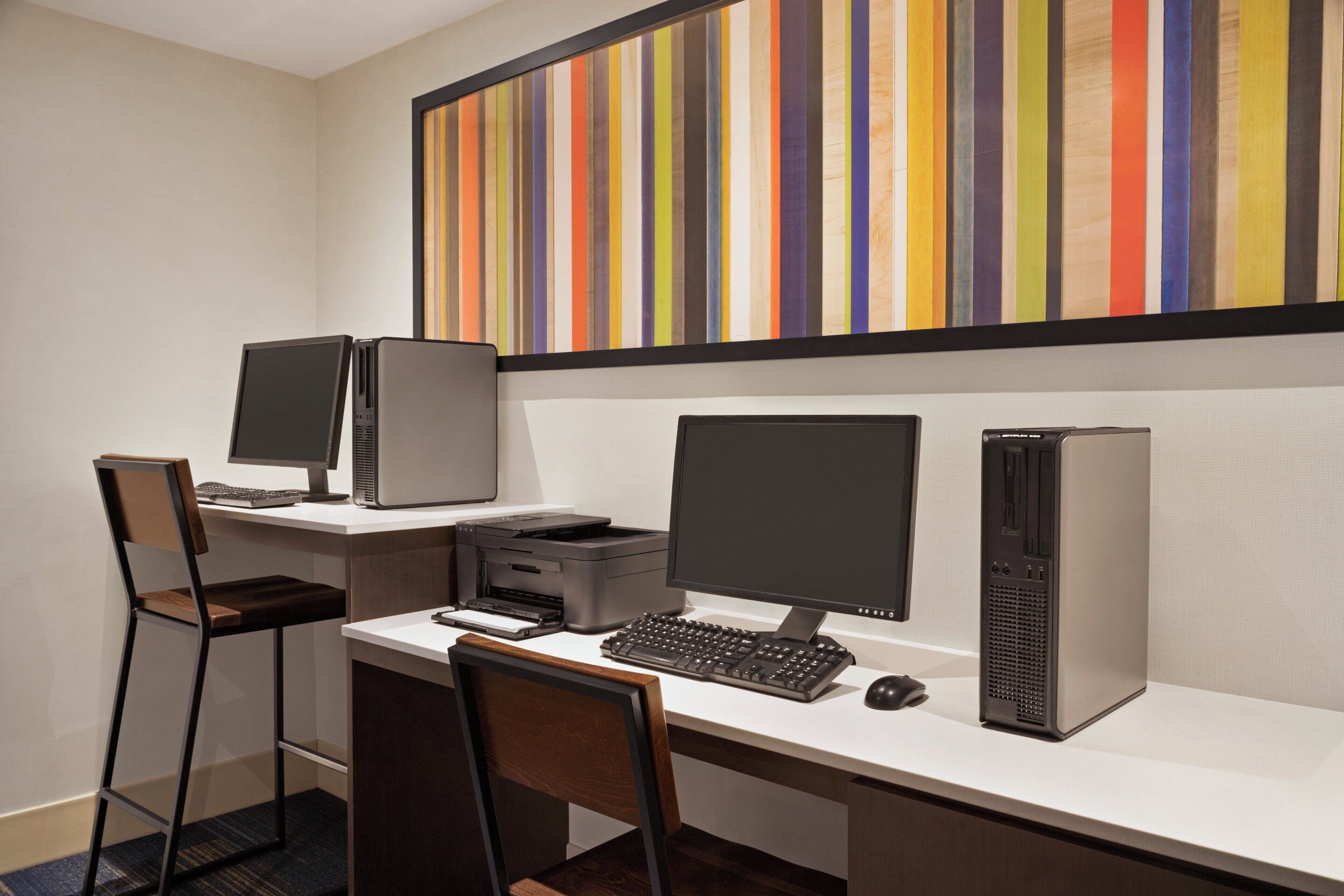 A workspace with two monitors, a desktop computer, a printer, and a keyboard.