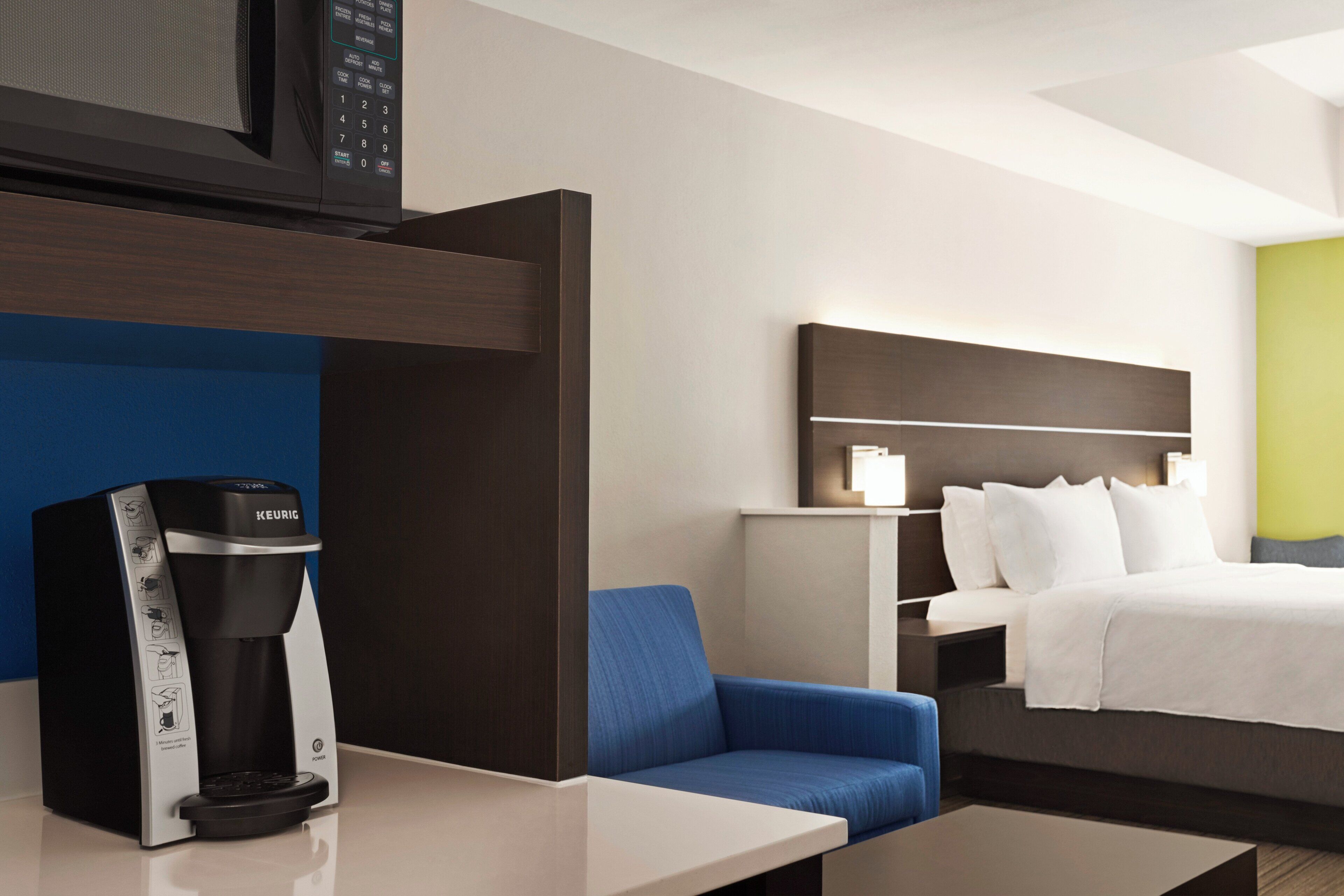 A hotel room with a bed, a coffee maker, a bedside table, and a nightstand.
