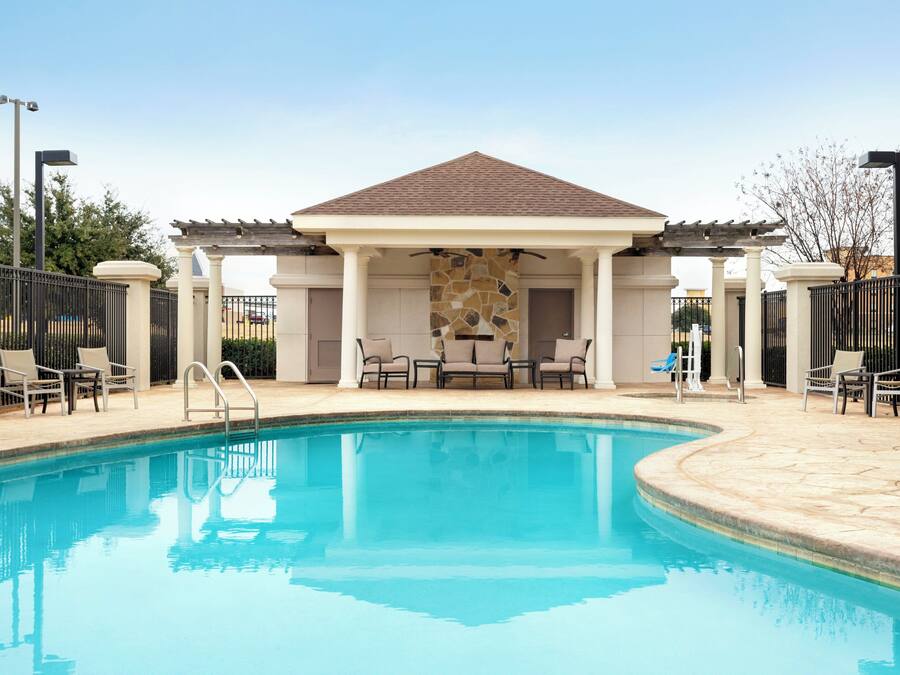 A swimming pool with a covered seating area and chairs.