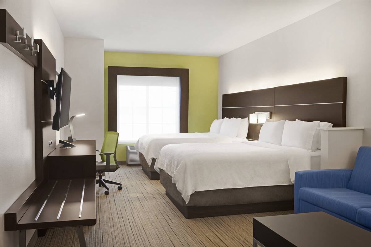 A hotel room with two beds, a desk with a computer, a TV, a chair, and a couch.
