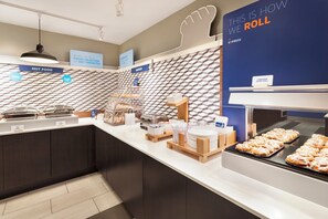 A breakfast buffet area with various food options, including a display for cinnamon sweet rolls.