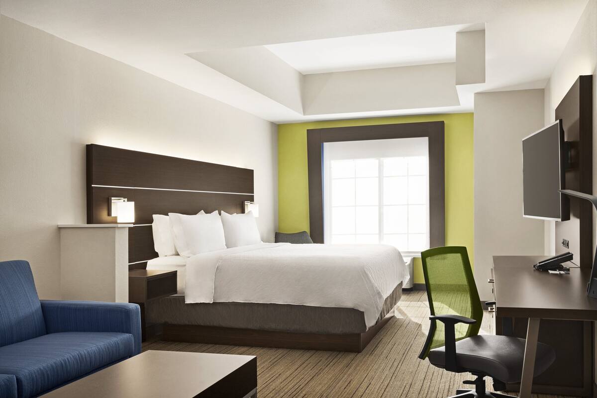A hotel room with a bed, a desk, a chair, a sofa, and a TV.