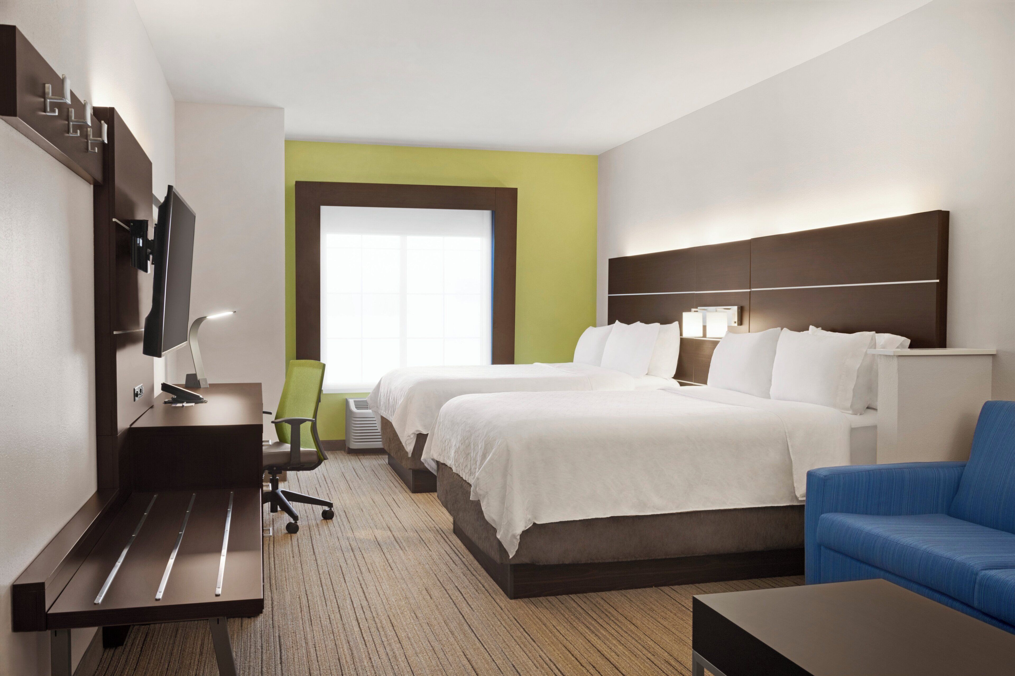 Una habitación de hotel con dos camas, un escritorio con silla, televisión y ventana.