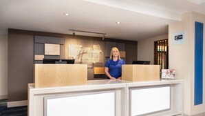 A hotel reception desk with a modern design, a digital display, and a sign indicating the hotel name.