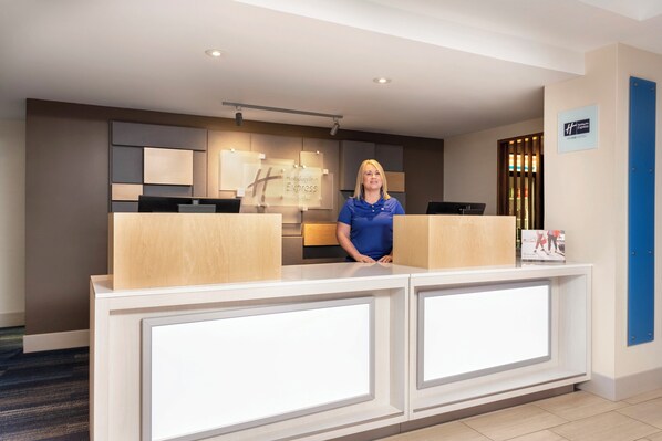 A hotel reception desk with a modern design, a digital display, and a sign indicating the hotel name.
