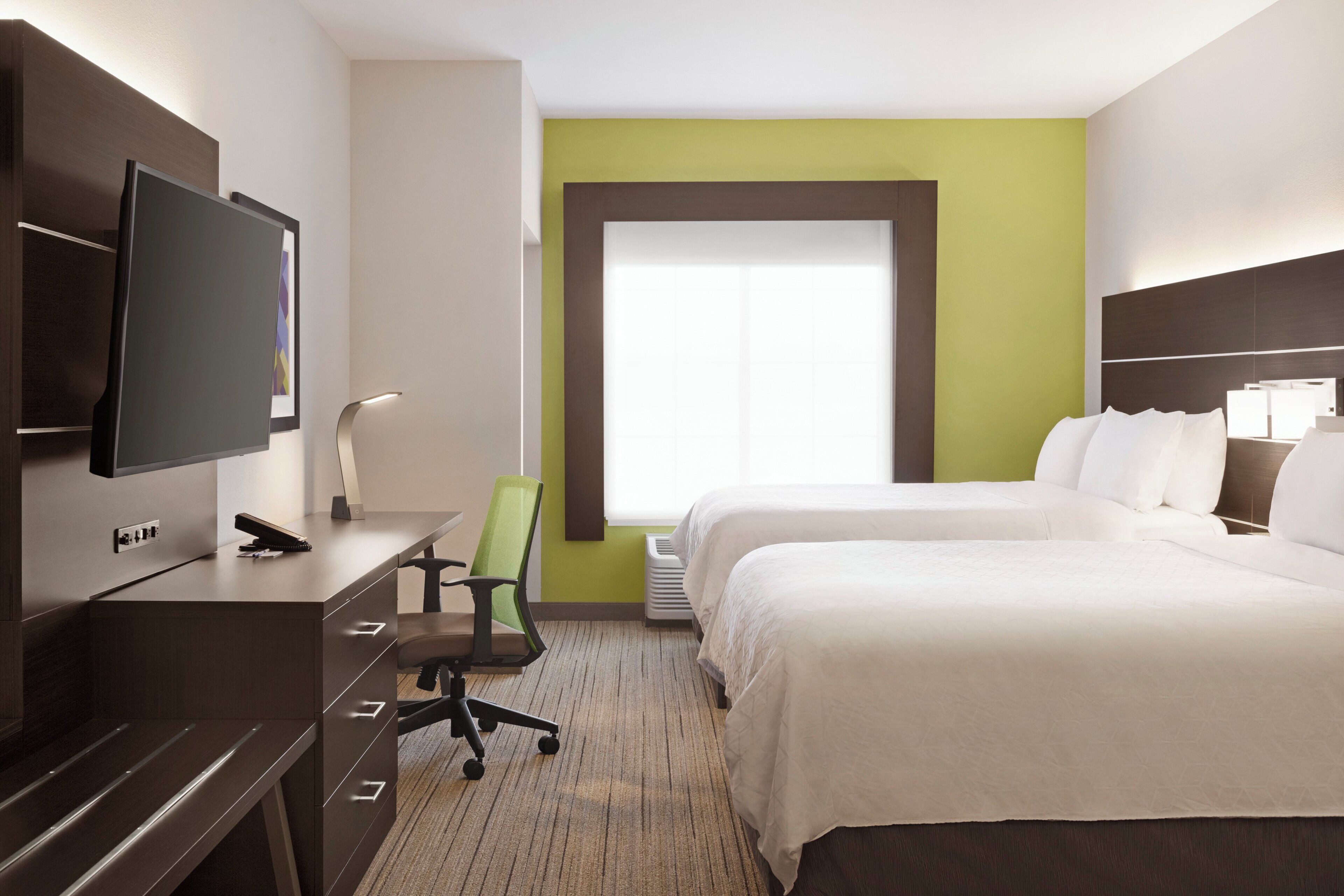 A hotel room with a bed, a desk with a chair, a television, and a window.