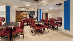 A modern dining area with red upholstered chairs, wooden tables, and a central coffee station.