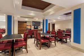 A modern dining area with red upholstered chairs, wooden tables, and a central coffee station. - Holiday Inn Express Hotel & Suites Durant by IHG (Durant)