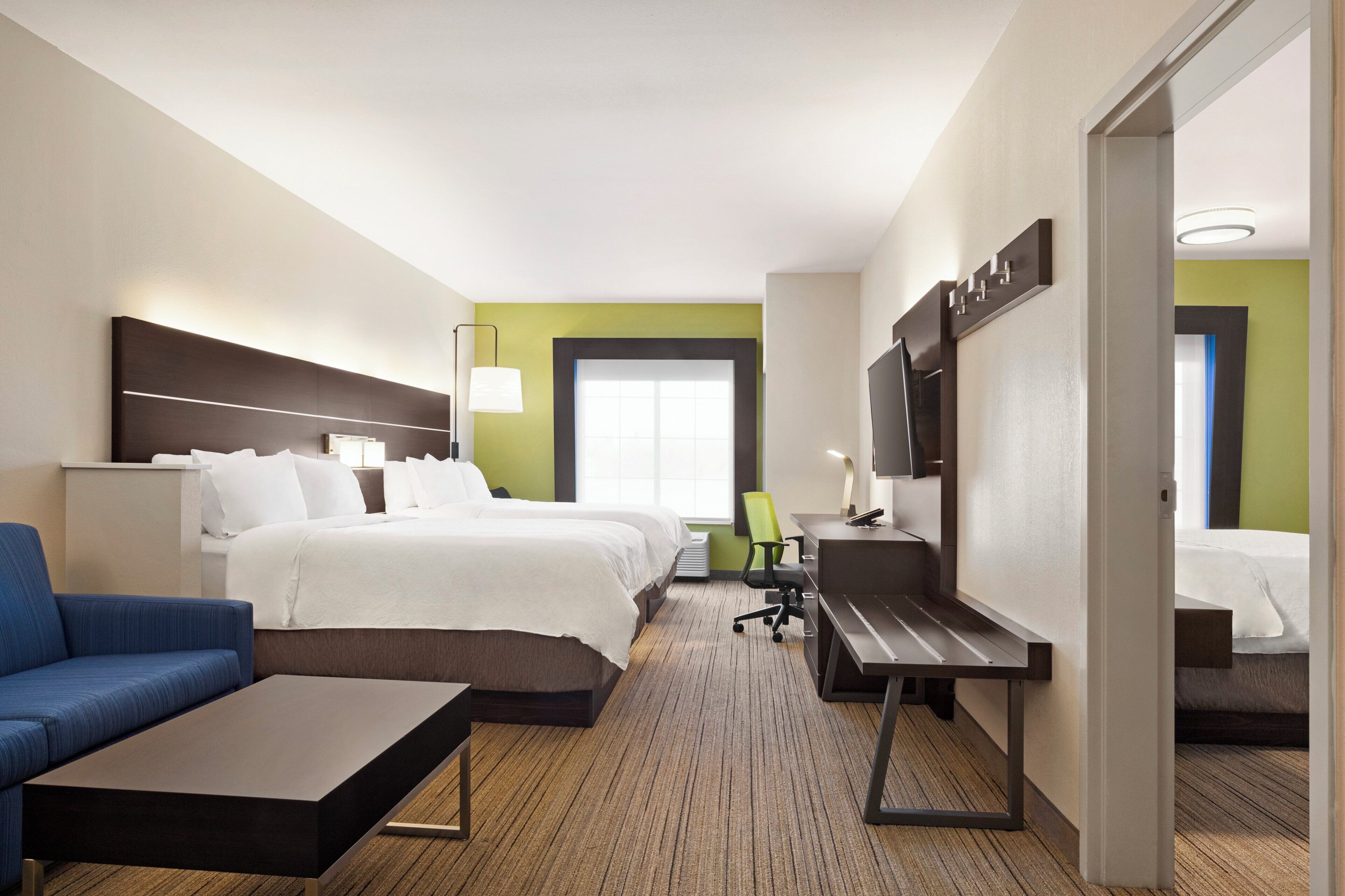 A hotel room with a bed, a desk, a chair, a sofa, and a television.
