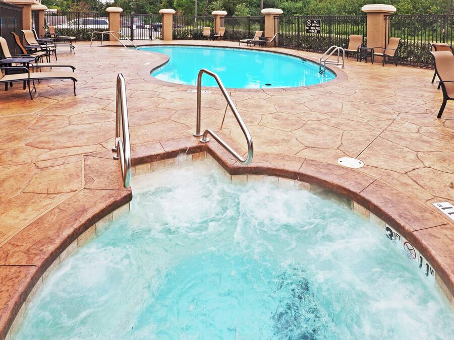 Un jacuzzi con escalera metálica, rodeado de sillones de descanso y una piscina.