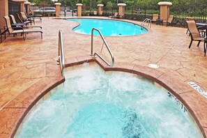 A hot tub with a metal ladder, surrounded by lounge chairs and a pool.