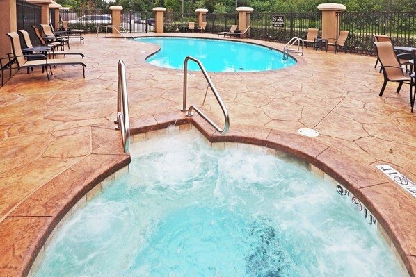 A hot tub with a metal ladder, surrounded by lounge chairs and a pool.