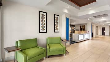 A hotel lobby with two green armchairs, a reception desk, and framed artwork on the walls.