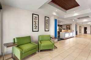 A hotel lobby with two green armchairs, a reception desk, and framed artwork on the walls.