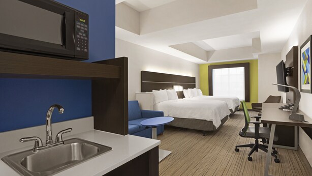 A hotel room with a kitchenette, a bed, a desk, and a small seating area.