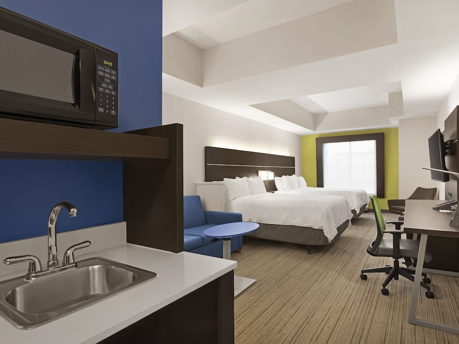 A hotel room with a kitchenette, a bed, a desk, and a small seating area.