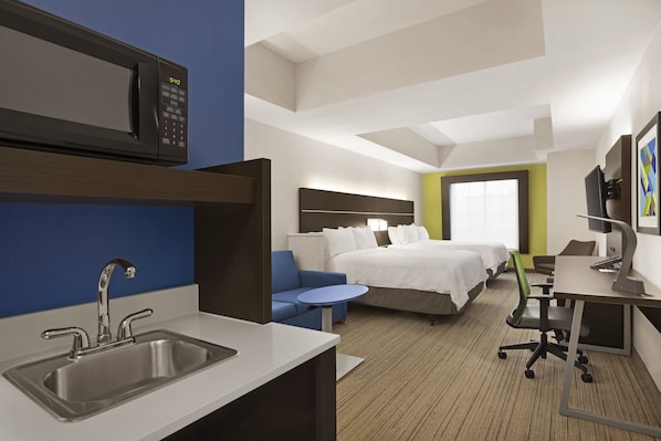 A hotel room with a kitchenette, a bed, a desk, and a small seating area.