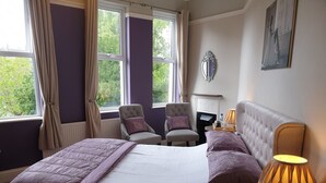 A bedroom with a bed, two armchairs, a side table with a lamp, a fireplace, and a window with curtains. - The Brandize Guest House (Torquay)