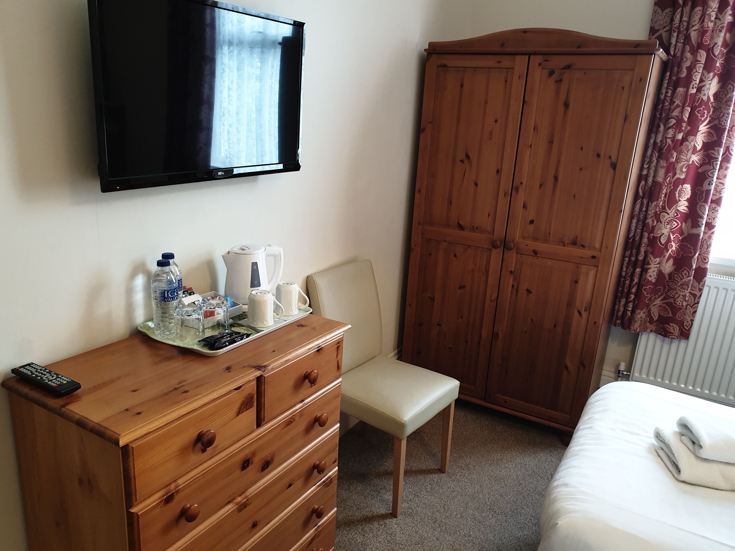 A hotel room with a wooden dresser, a television, a wardrobe, a bed, and a chair.