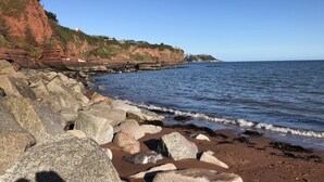 A rocky coastline with a clear view of the sea and a cliff with buildings on top. - The Brandize Guest House (Torquay)