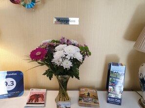 A reception desk with a sign, a vase of flowers, brochures, and a brandize award plaque. - The Brandize Guest House (Torquay)
