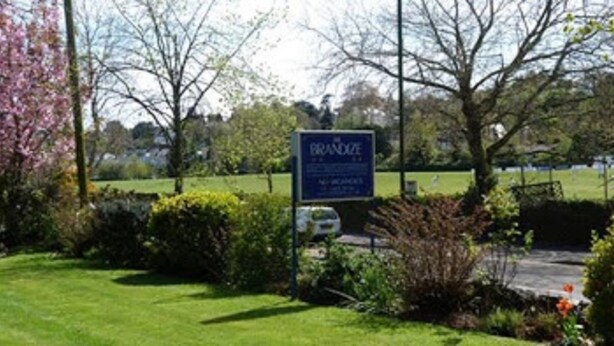 A sign for a hotel named "Branice" with a view of a park and a body of water in the background. - The Brandize Guest House (Torquay)