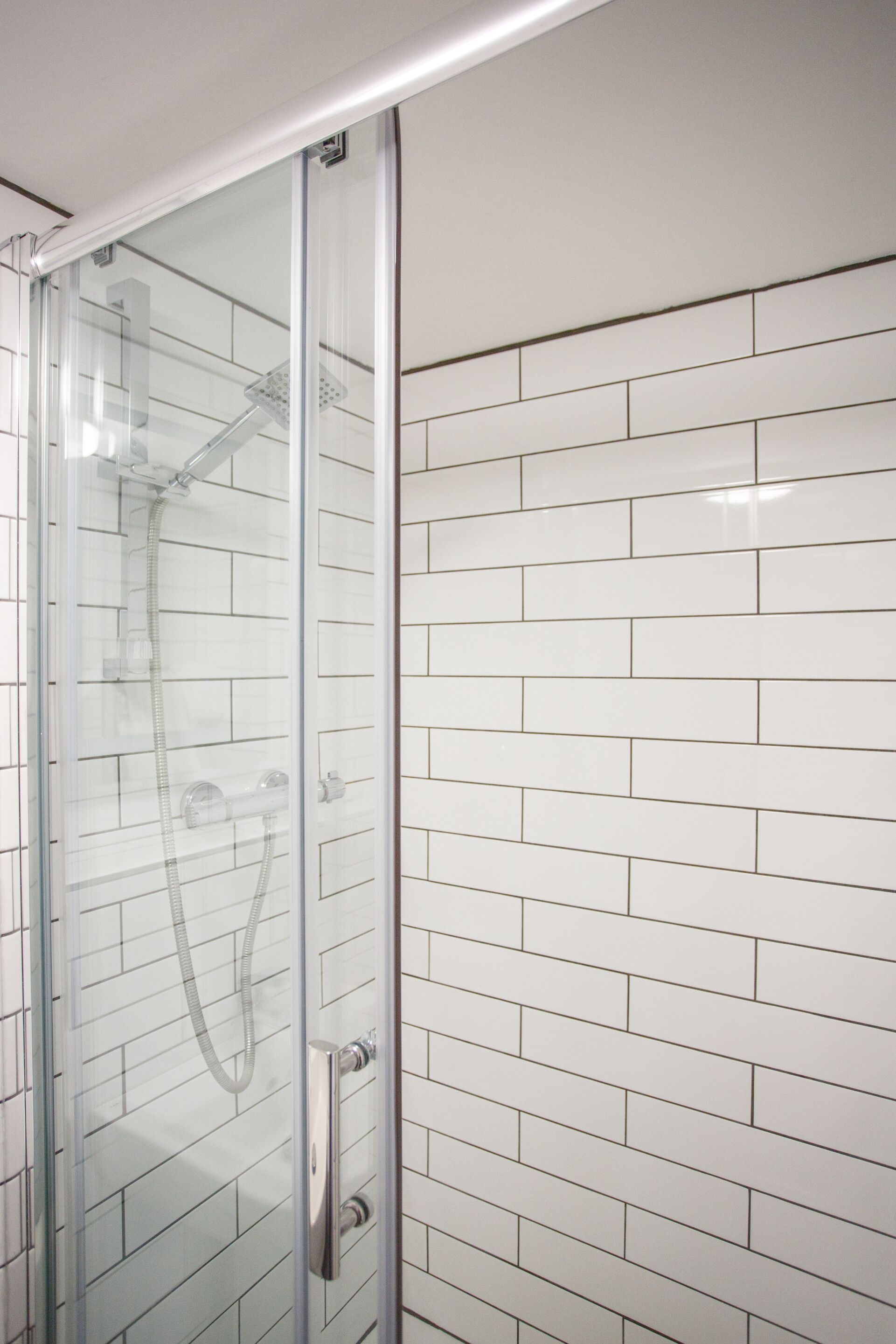 Ducha envuelta en vidrio con cabezal de ducha de mano y panel de control en la pared.