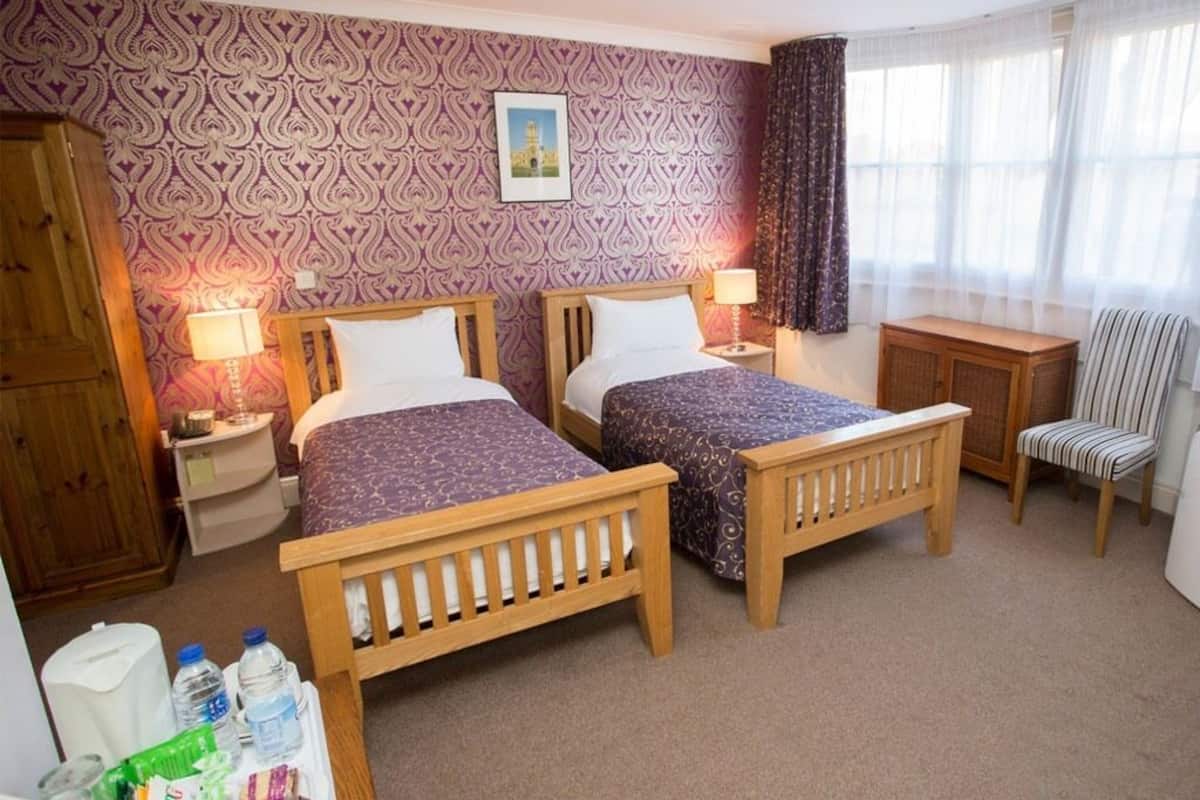 A hotel room with two wooden beds, a small desk, a chair, and a wardrobe.