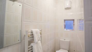 Une salle de bain avec des murs carrelés de carreaux blancs, des toilettes, une fenêtre donnant sur un beau paysage et un porte-serviettes avec une serviette blanche.
