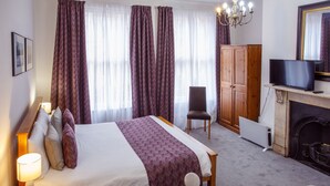 A hotel room with a large bed, a wooden wardrobe, a television, and a fireplace. - The Buttery Hotel (Oxford)