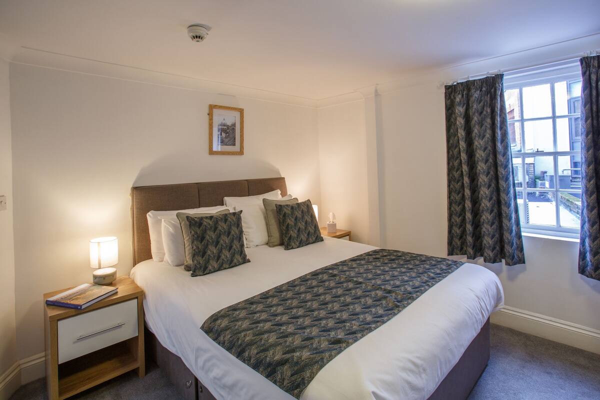 A neatly made bed with a patterned bedspread, a bedside lamp, and a framed picture on the wall.