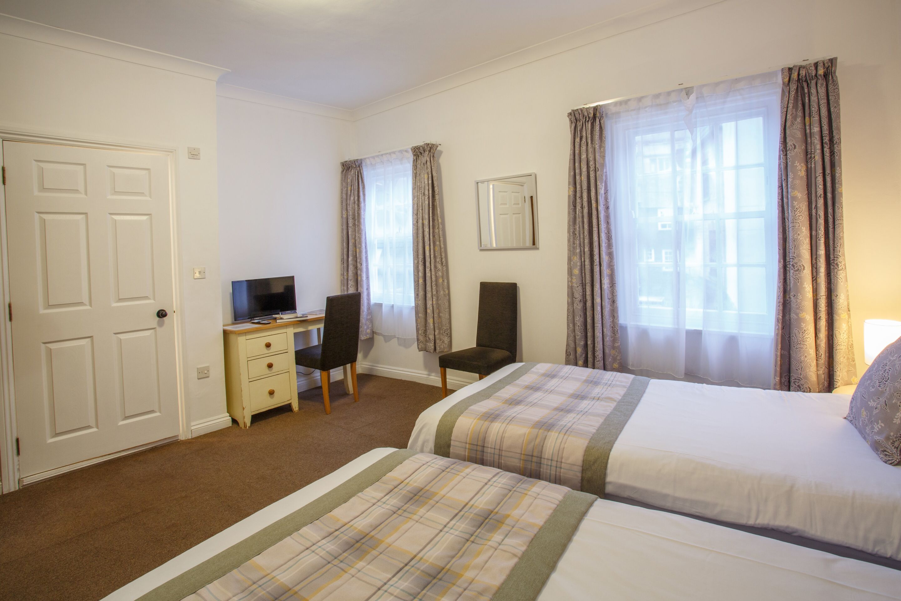 A hotel room with two beds, a desk with a chair, a television, and a door.