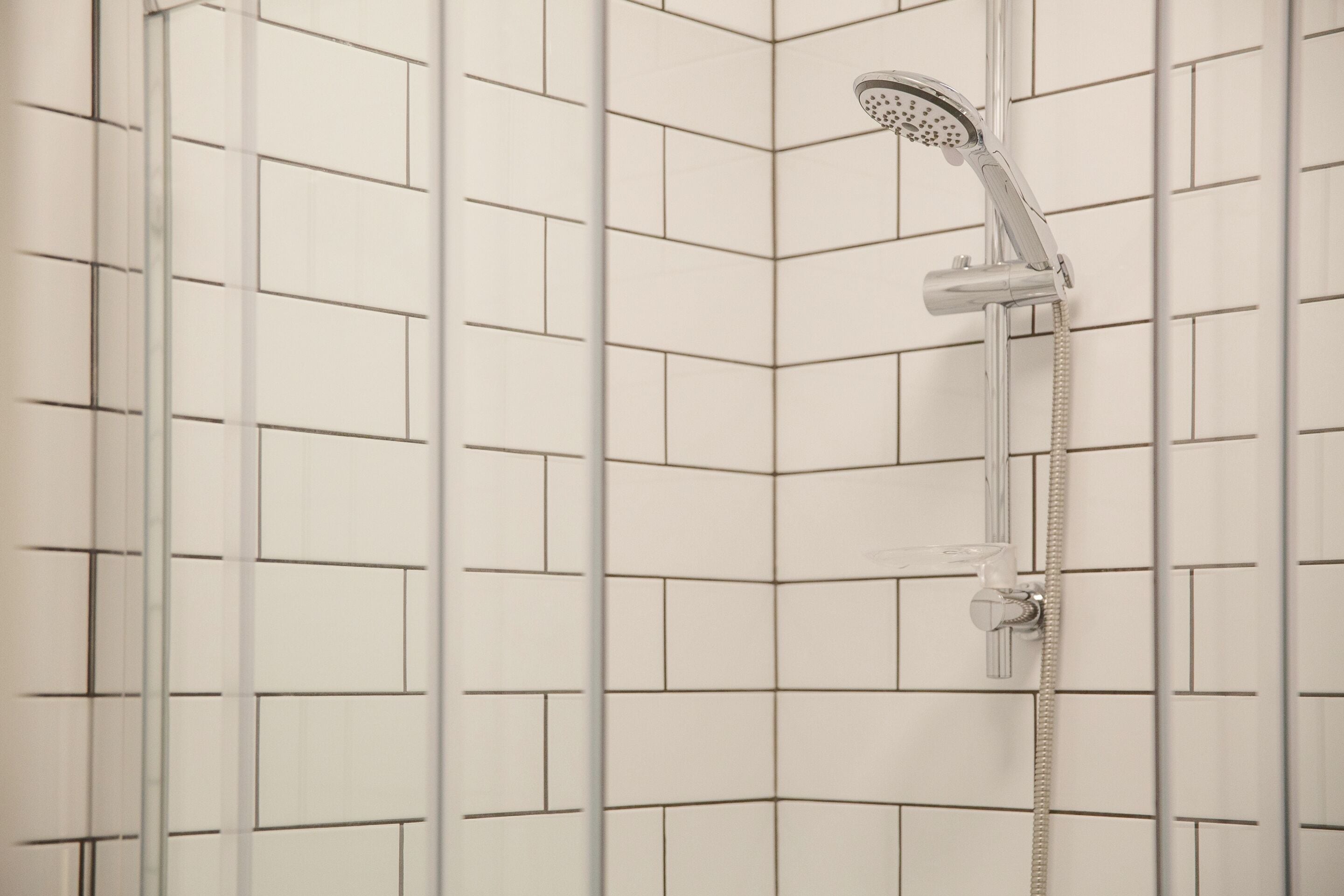 A shower with a handheld showerhead and a wall-mounted control.